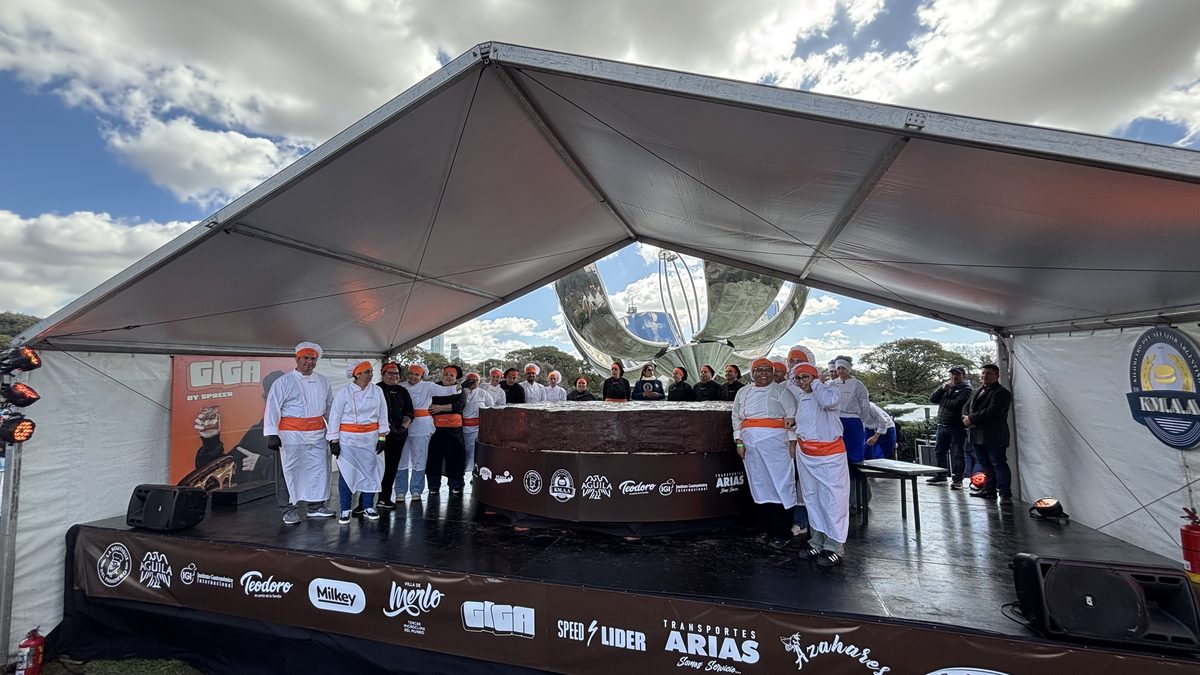 Equipo del IGI con uniforme junto al alfajor gigante sobre el escenario, con la Floralis Genérica de fondo
