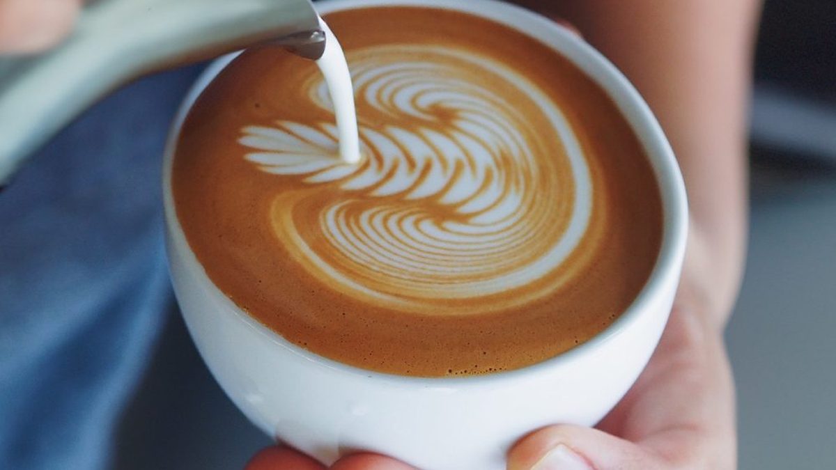 Barista vertiendo leche texturizada sobre un café para dibujar arte latte en la taza