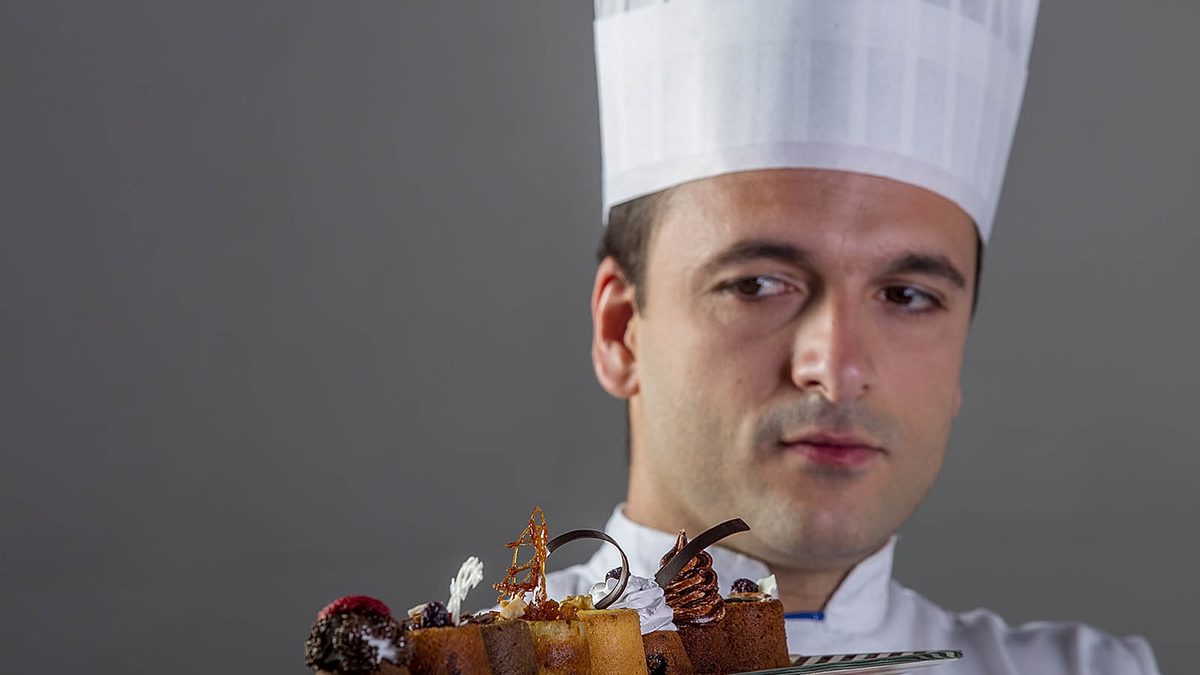 Chef pastelero con gorro observando una bandeja de petit fours decorados con chocolate templado y caramelo