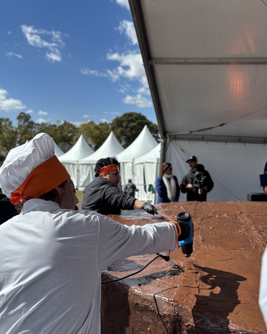 Pastelera del IGI trabajando la cobertura de chocolate sobre el borde del alfajor gigante al aire libre