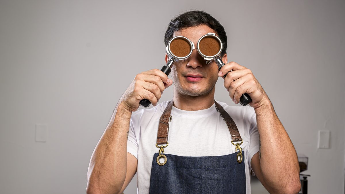 Barista con delantal sosteniendo dos portafiltros cargados de café molido frente a la máquina de espresso