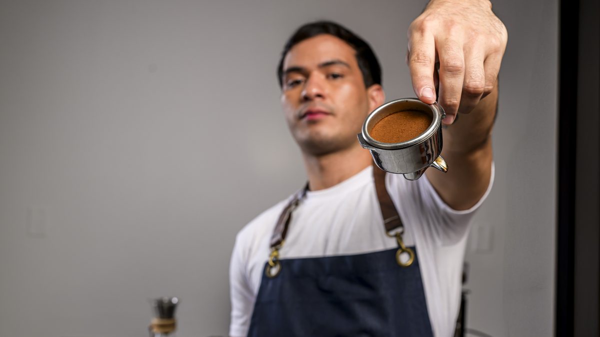 Barista de IGI mostrando una taza de café recién preparada frente a la máquina de espresso