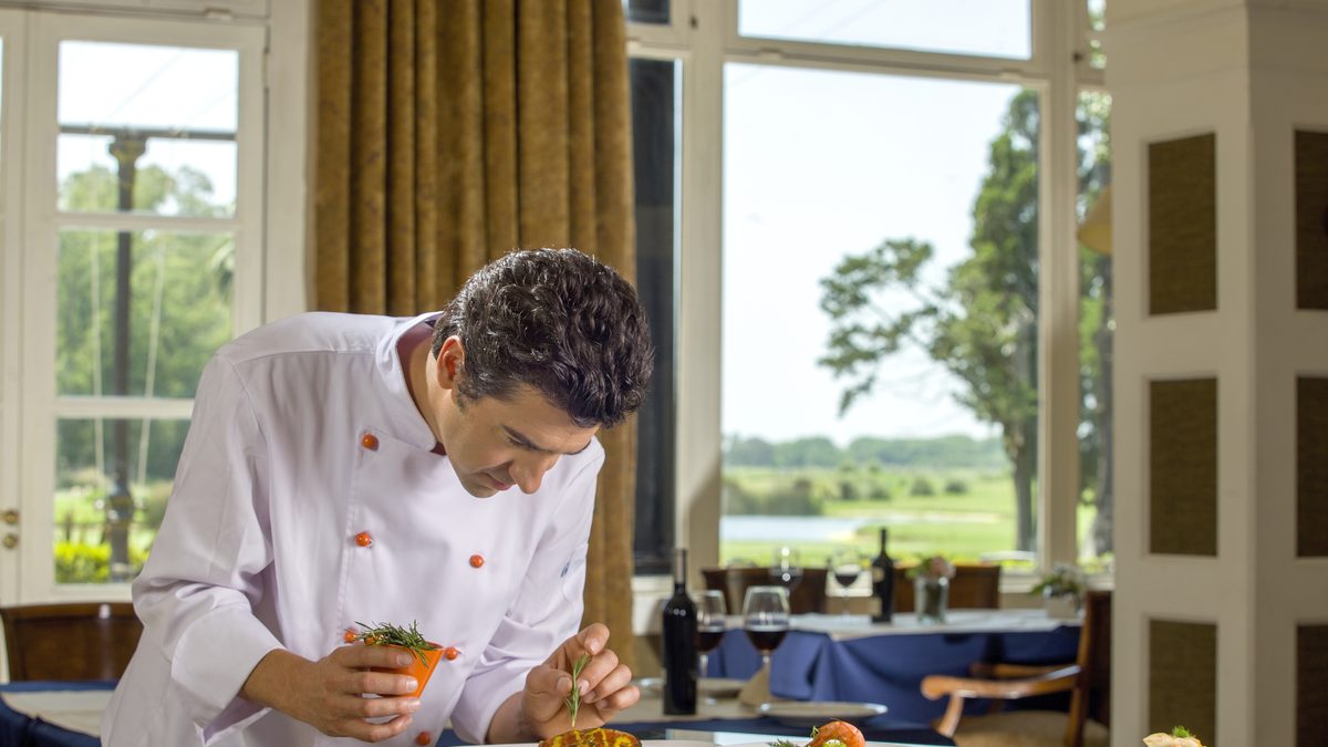 Chef de IGI terminando un plato en el salón de un restaurante, con la barra de servicio al fondo
