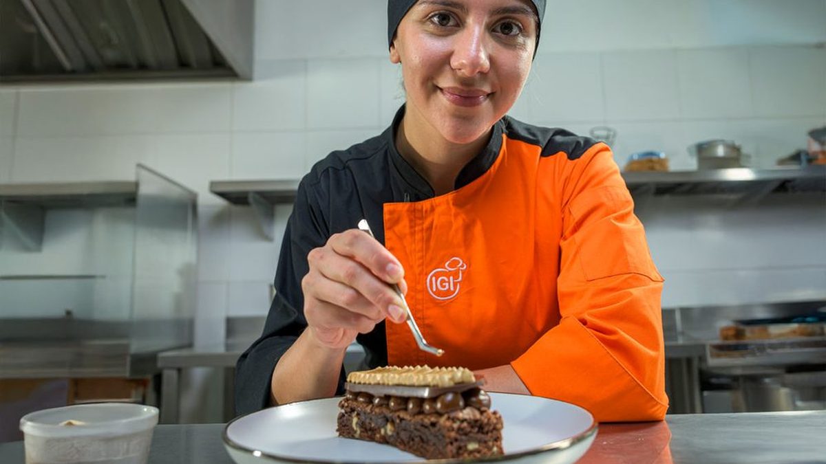 Pastelera con uniforme de IGI terminando la decoración de un postre de chocolate en una cocina profesional