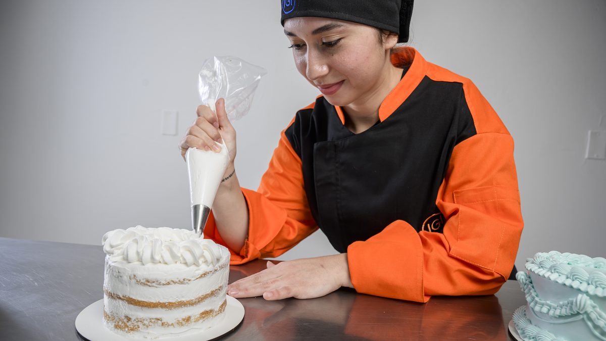 Alumna de IGI decorando una torta con manga pastelera en una clase de pastelería