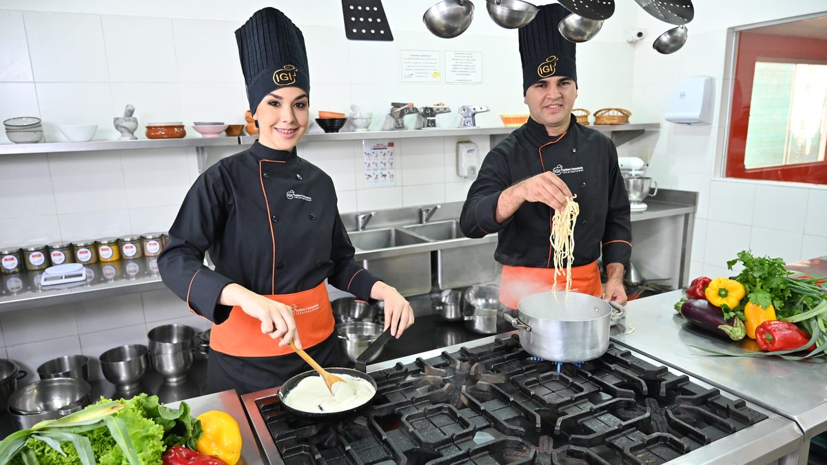 Dos estudiantes de IGI con uniforme cocinando pastas en una cocina profesional