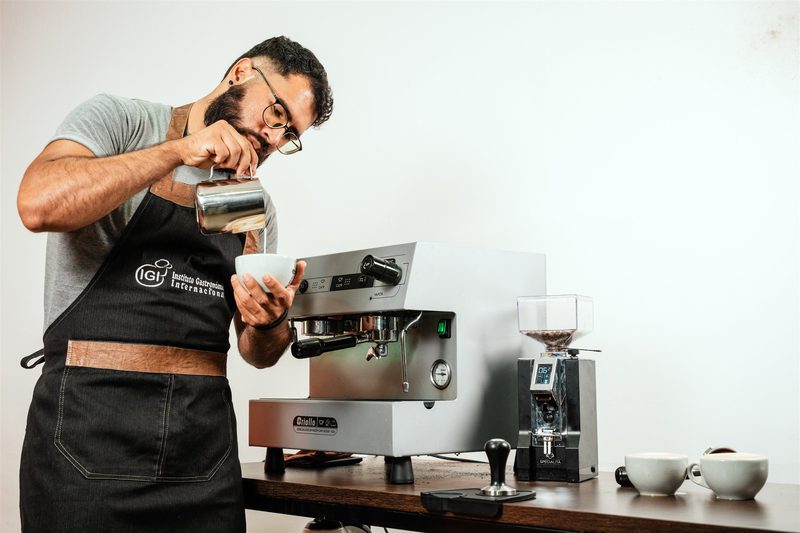 Barista preparando una bebida con leche junto a una máquina de espresso