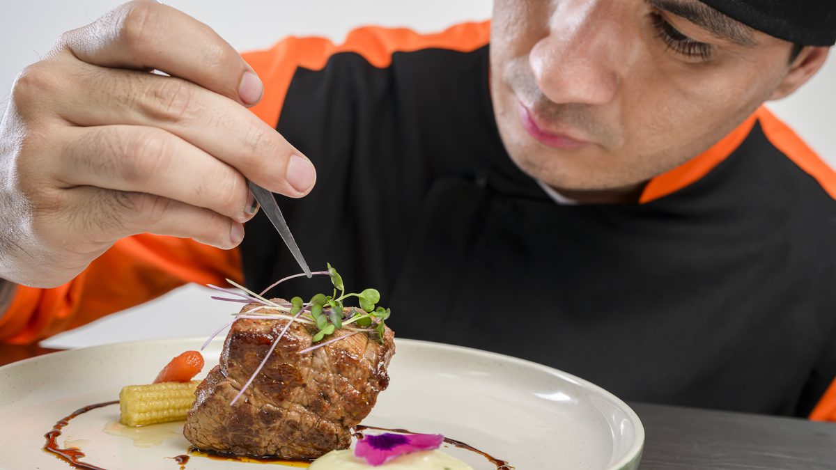 Chef de IGI terminando un plato con pinza de emplatado durante una clase práctica