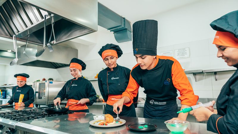 Grupo de alumnos de IGI emplatando junto al chef instructor en una clase práctica de cocina